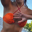 Bikini model wearing Cherry Crush reversible triangle top by Bikini Flavors. Orange reverses to red with interchangeable string ties! American made.