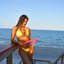 Bikini model at beach wearing Bikini Flavors reversible swimsuit in Strawberry Sunrise. Hope is holding thicker swimsuit straps in her hand.
