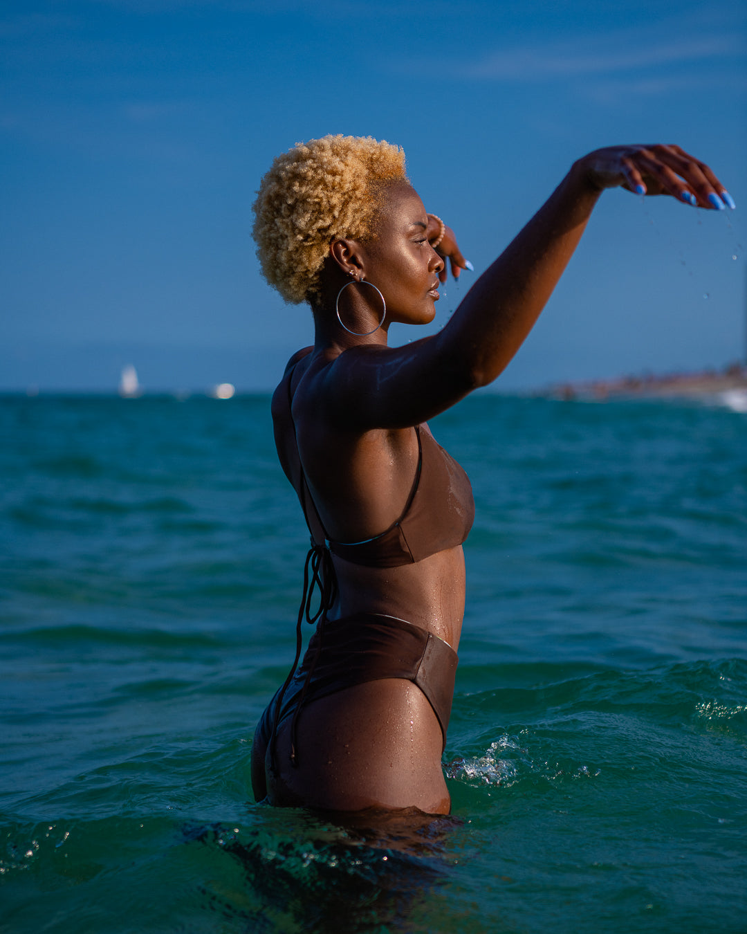 Bikini model standing in ocean, wearing Bikini Flavors reversible cross-back top and high waist cheeky bikini bottoms in Matcha. American Made.